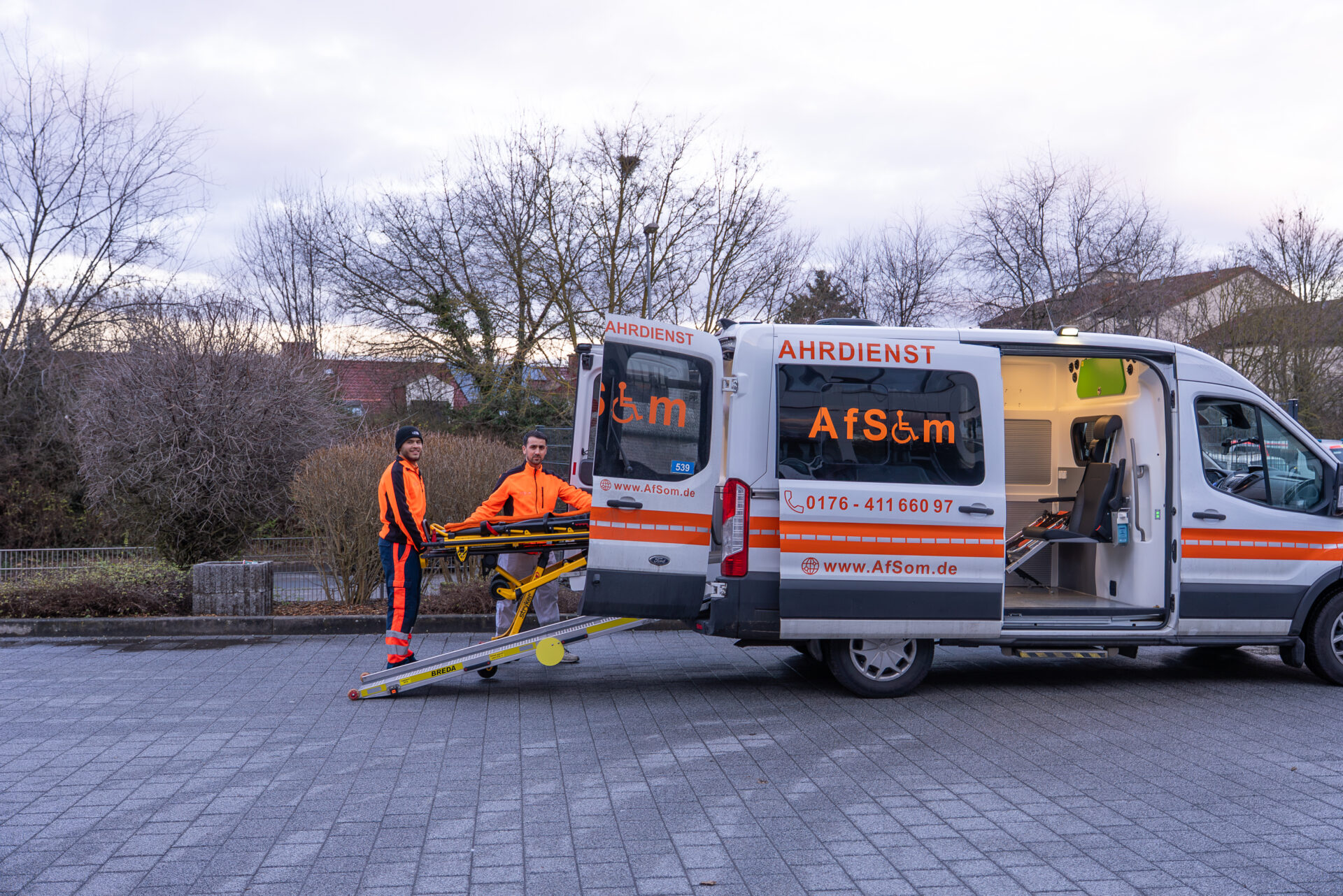 AfSom Fahrer helfen einer Patientin über die Rampe in den rollstuhlgerechten Krankenfahrdienst-Transporter